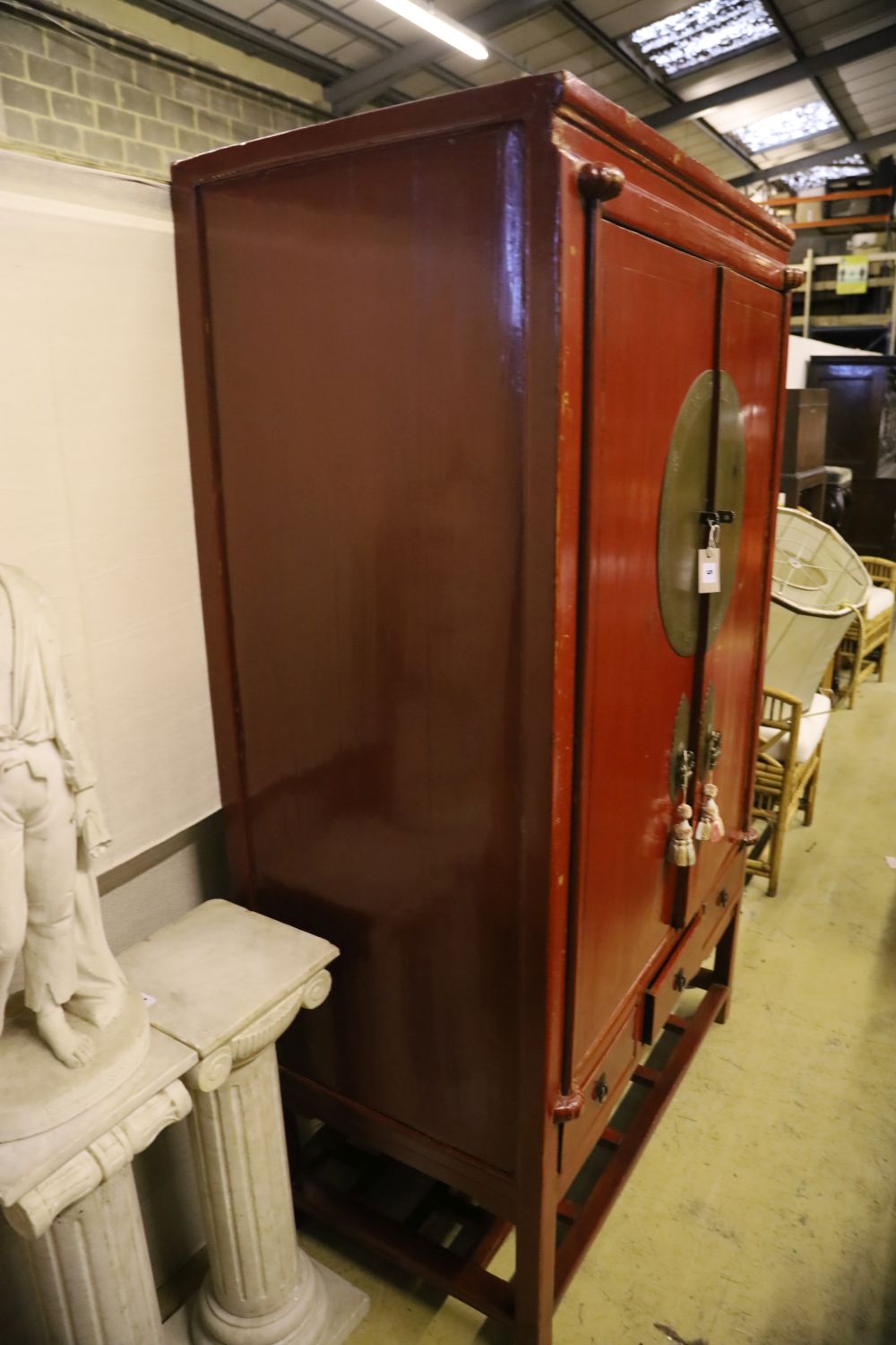 A Chinese two-door brass-mounted red-lacquered cupboard fitted three short drawers over an open shelf, width 110cm, depth 60cm, height